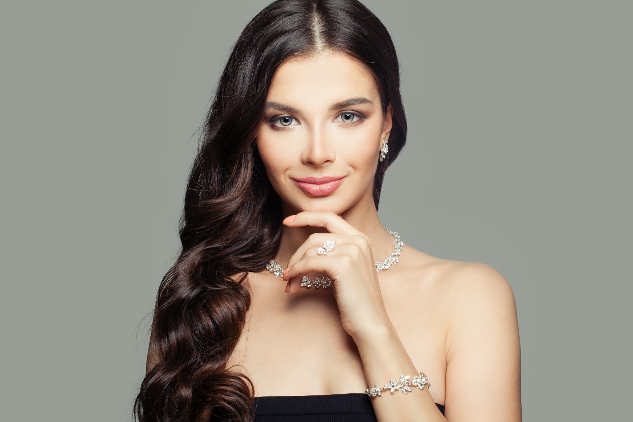A woman with long dark hair poses wearing a matching white diamond necklace set.