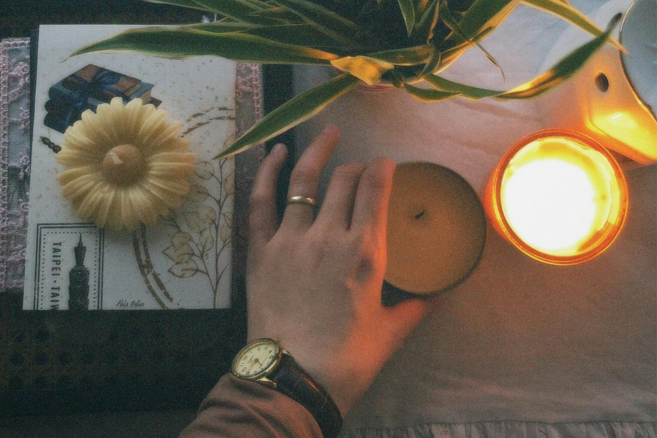 a person’s hand placing a candle on a table, wearing a vintage-inspired watch
