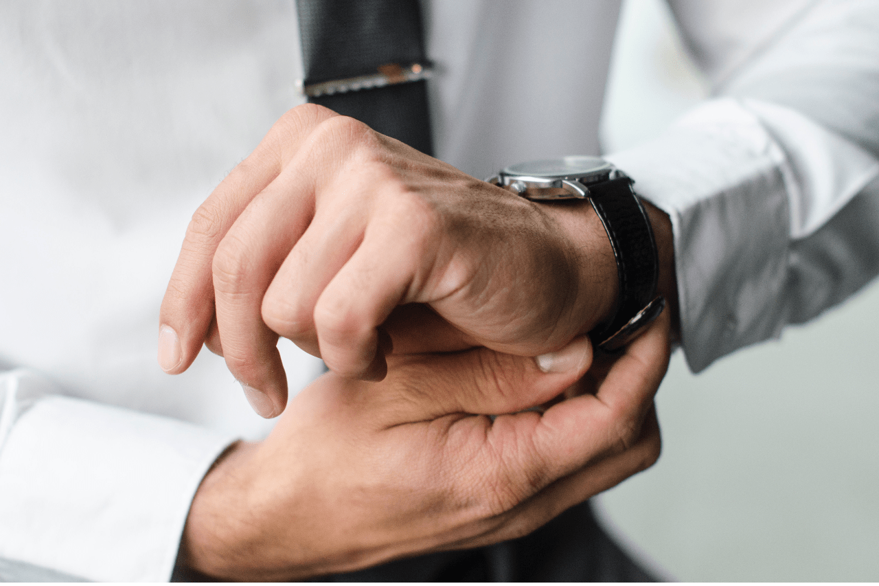 A close up of a man’s hand in white shirt, while he fixing his wristwatch with dark leather strap