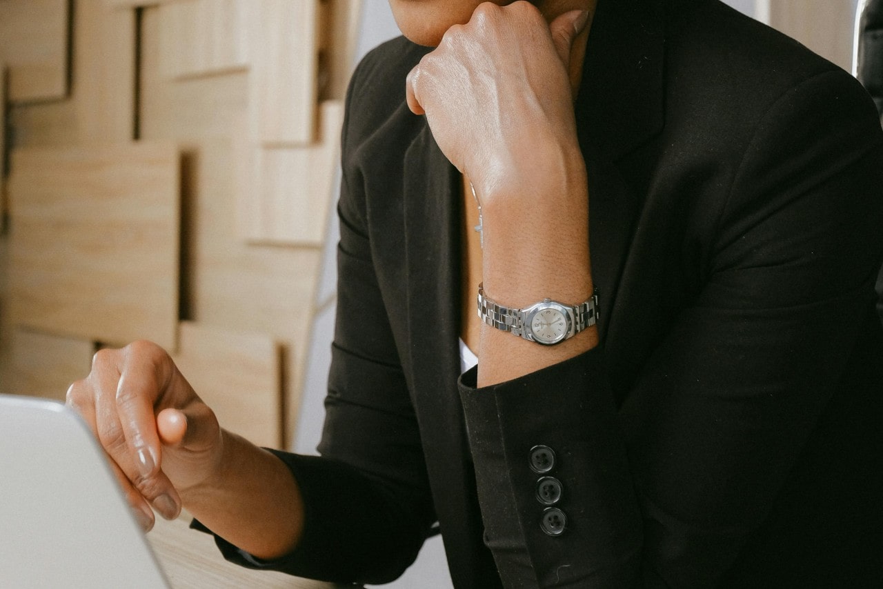 A close up of a woman wearing a stainless steel wristwatch while working at a desk on a laptop.