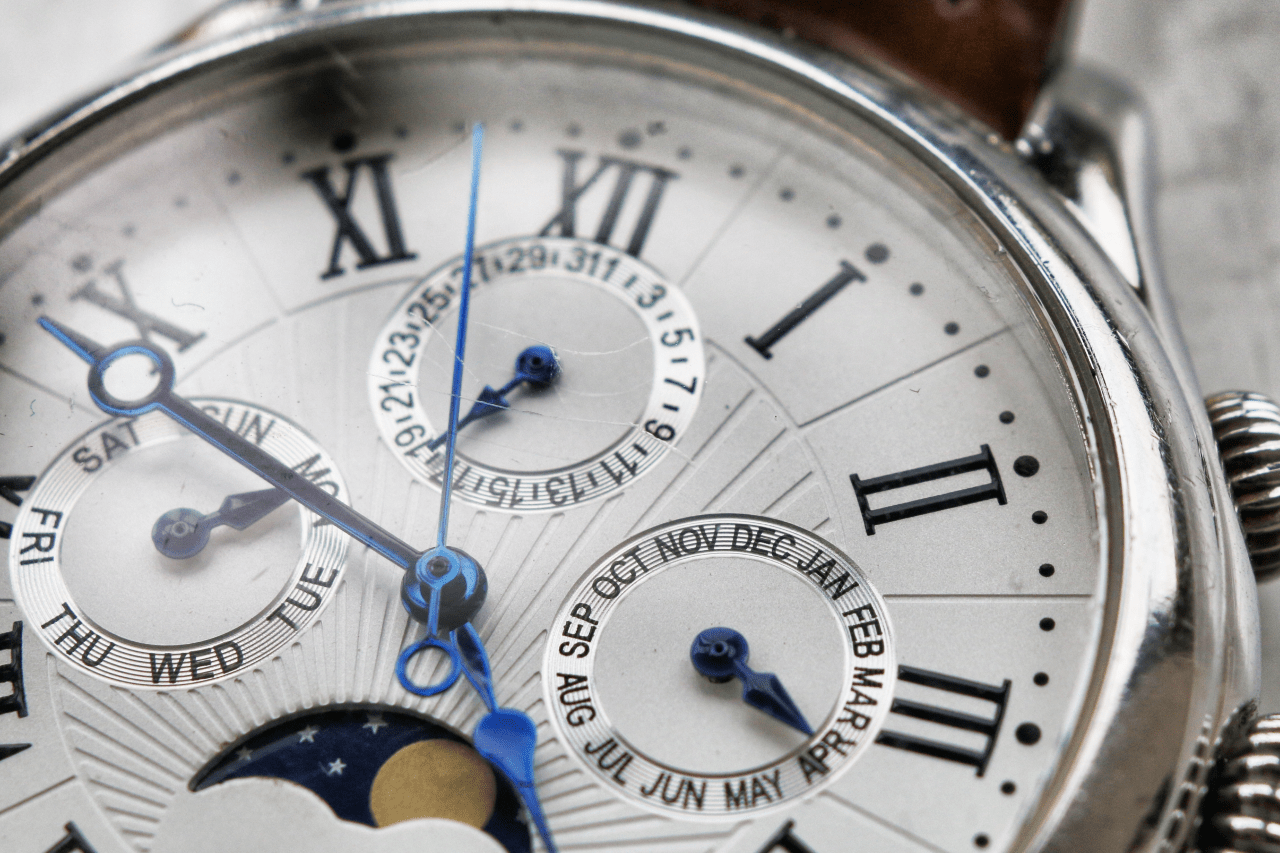 A close-up of a watch dial featuring Roman numerals and multiple subdials, with blue hands and intricate detailing.