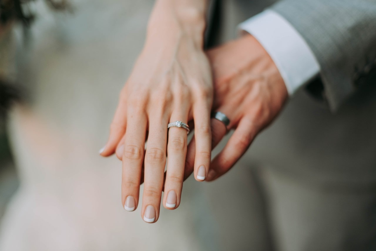 A close up of a bride’s and groom’s hands, showcasing white gold wedding bands.