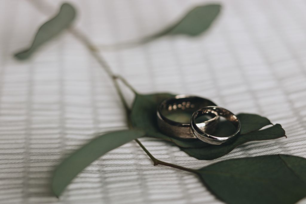 A close up of two yellow gold wedding bands resting on a leaf