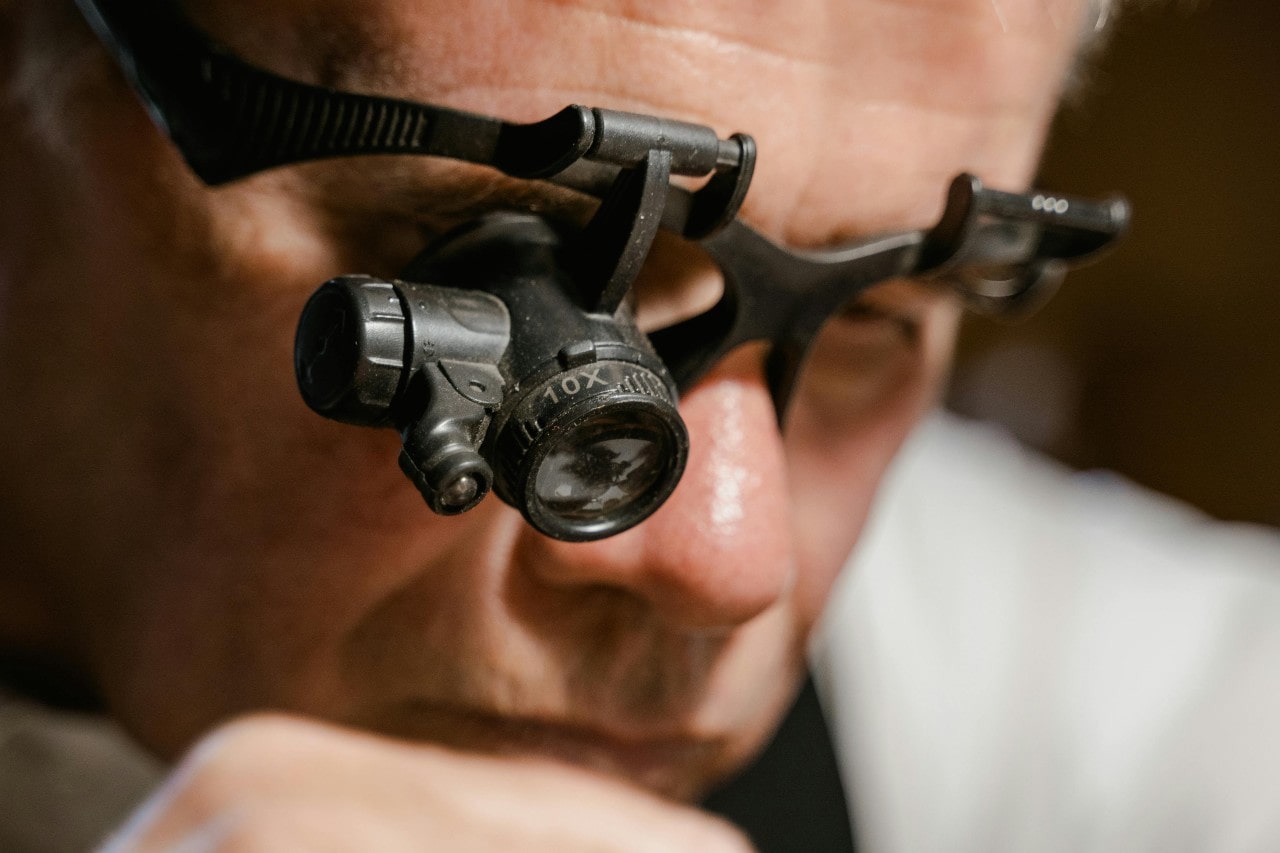 A close-up of a jeweller wearing jewellers glasses as they make a repair.