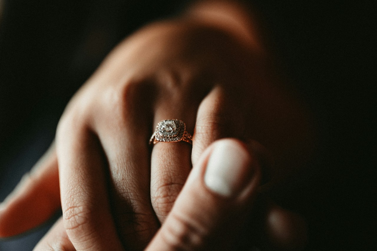 A close up of women’s hand held by men’s hand, showcasing rose gold double halo engagement ring.