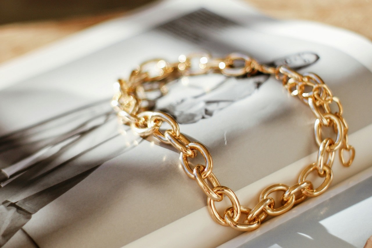 A gold chain bracelet rests elegantly on the pages of a fashion magazine. A gold chain bracelet rests elegantly on the pages of a fashion magazine.