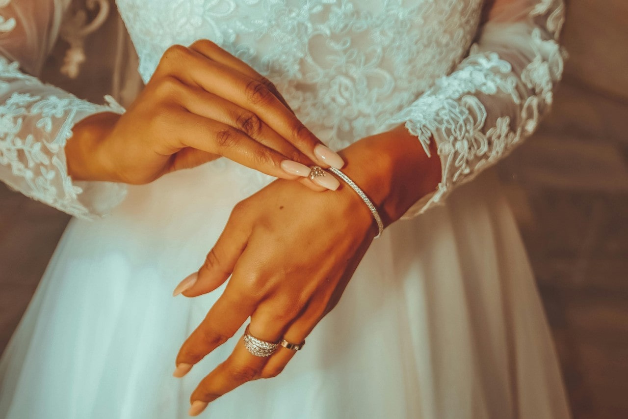 A bride adjusts a delicate diamond bracelet while wearing a lace-sleeved wedding gown A bride adjusts a delicate diamond bracelet while wearing a lace-sleeved wedding gown