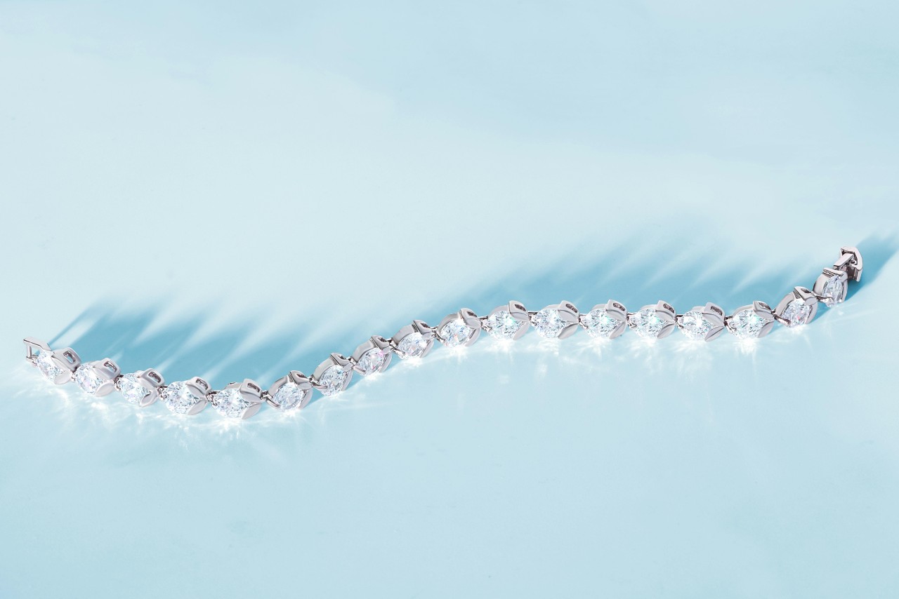 A white gold diamond tennis bracelet rests on a blue surface A white gold diamond tennis bracelet rests on a blue surface