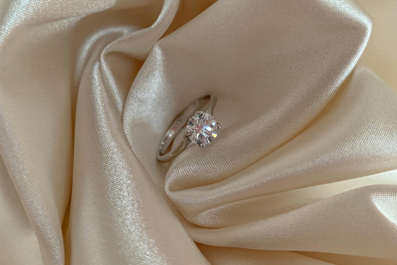 A white gold round cut solitaire engagement ring on a white atlas fabric A white gold round cut solitaire engagement ring on a white atlas fabric