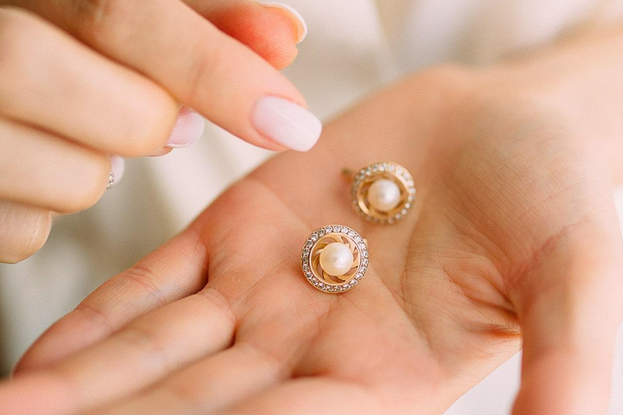 Pearl and halo studs held in the palm of a woman’s hand