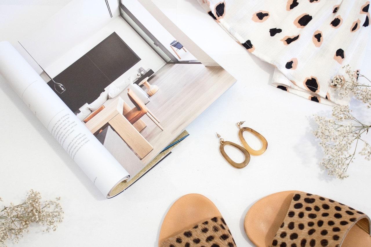 Pair of drop earrings on a table accompanied by a magazine, sandals, and flowers