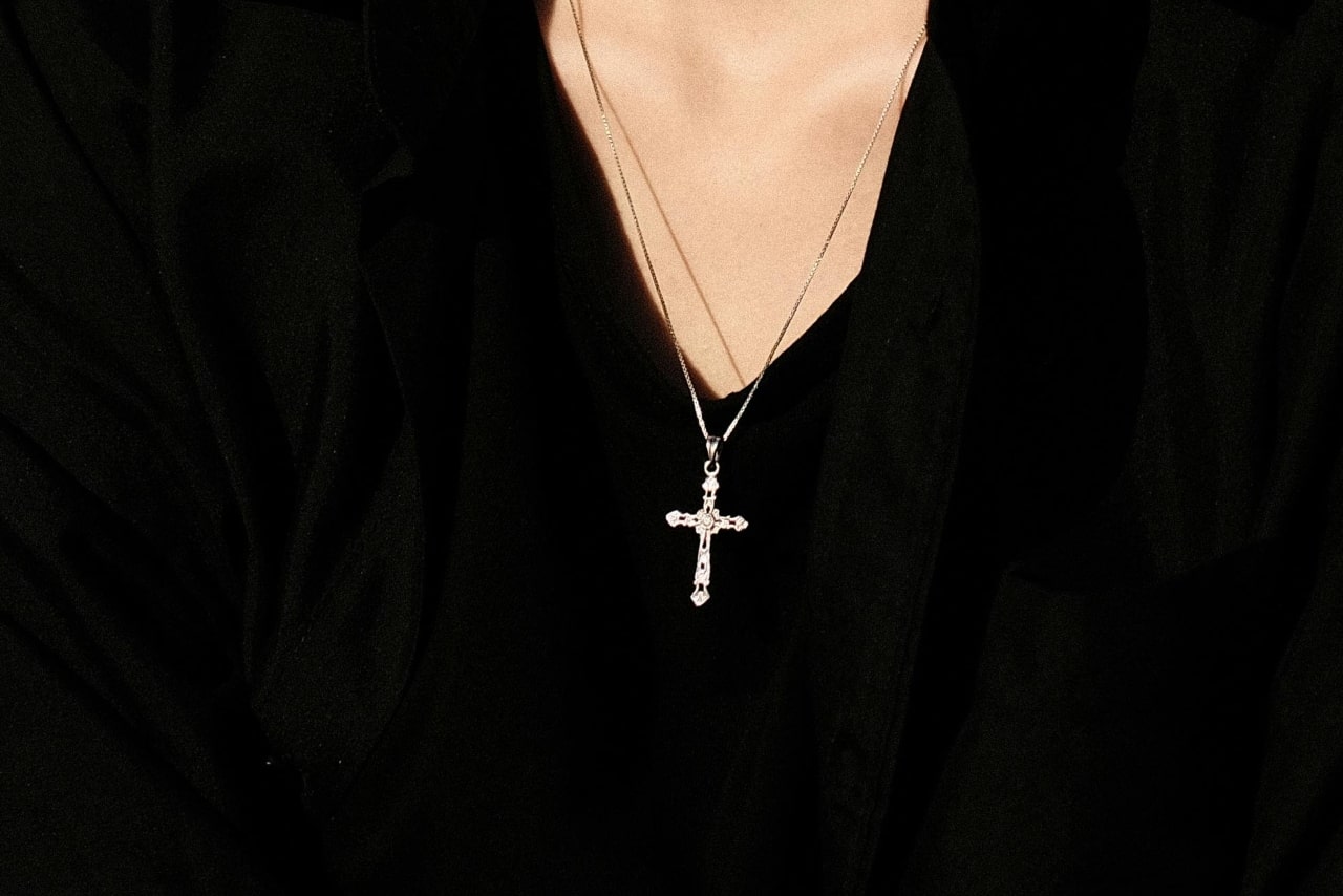 A close-up of a yellow gold cross pendant against a black blouse.