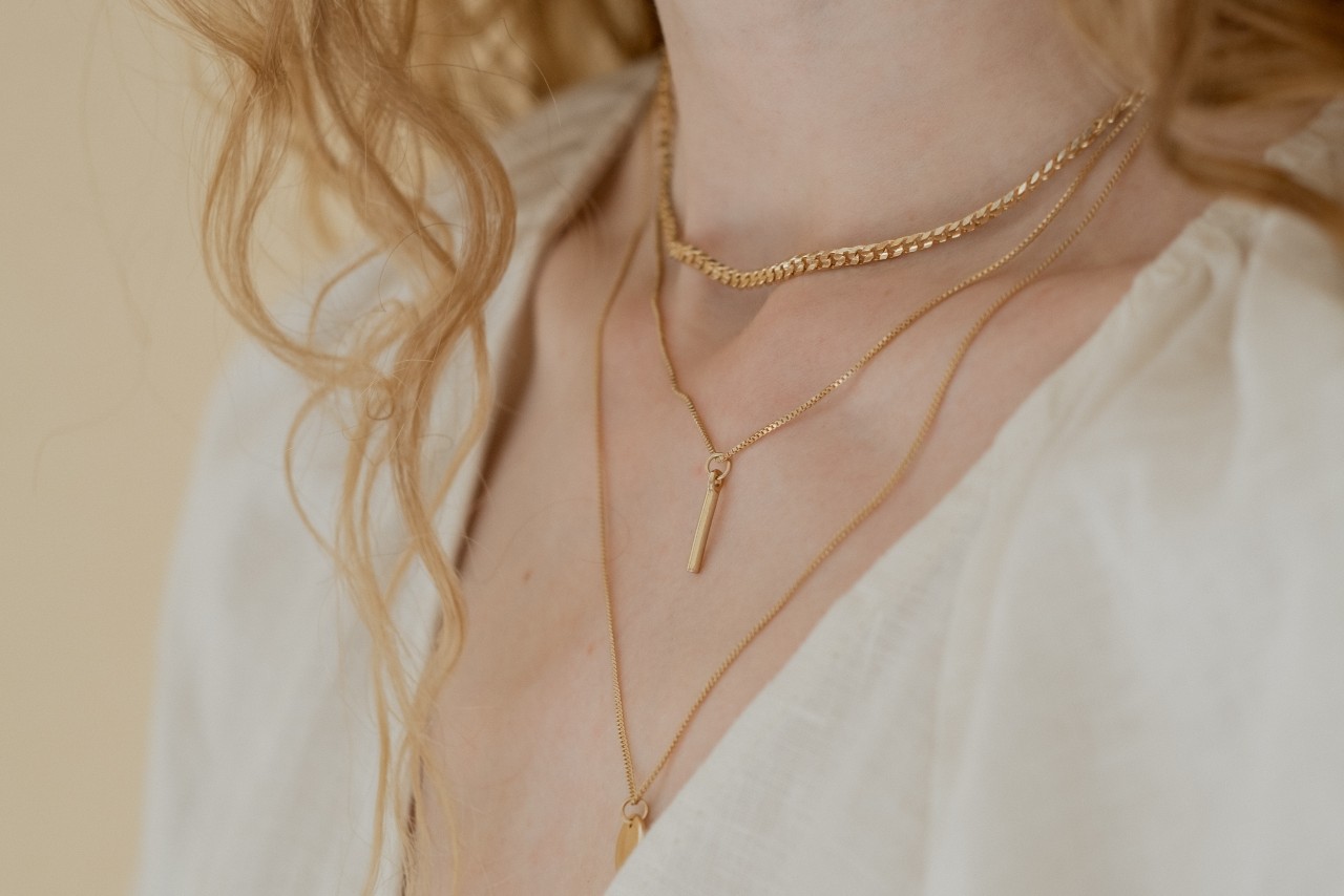 A close up of a layered yellow gold necklace on a woman’s neck in the white blouse. A close up of a layered yellow gold necklace on a woman’s neck in the white blouse.