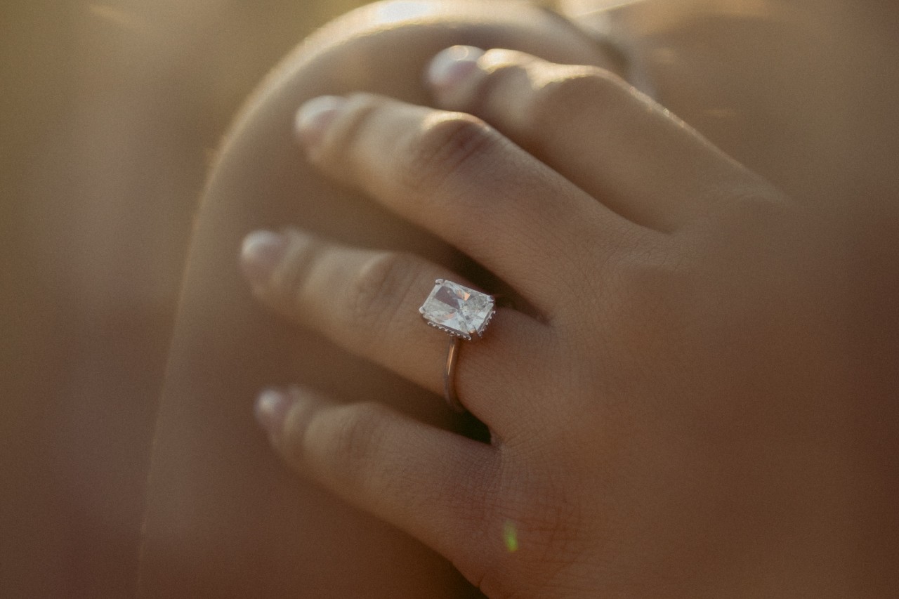 a woman’s hand resting on her shoulder and wearing a diamond solitaire engagement ring