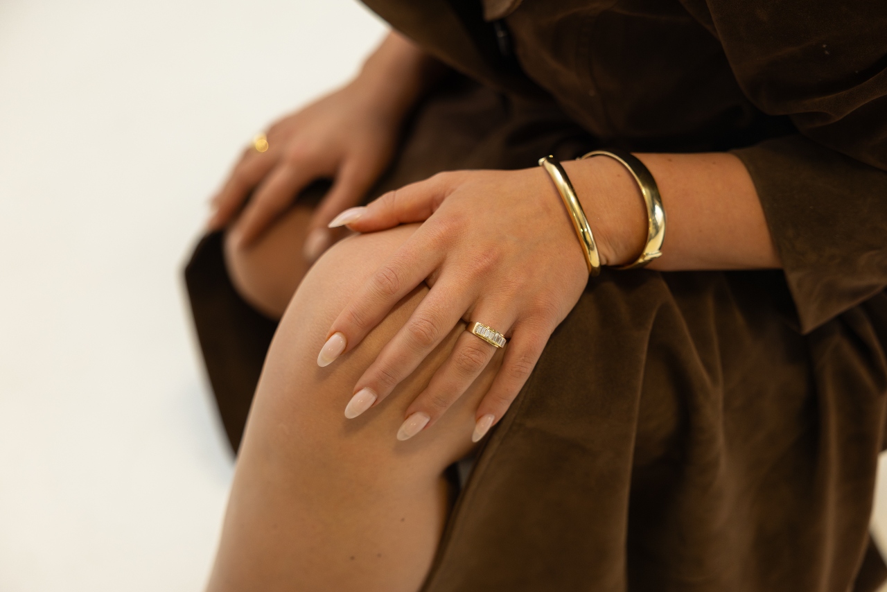 A close-up view on a woman’s five-diamond band and two all yellow gold bangles that have a wider design that hugs the person’s wrist.