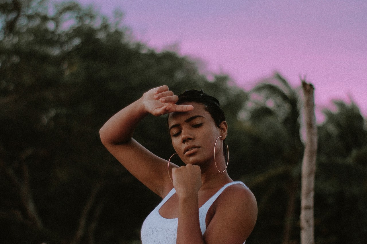 A wide view of a young woman wearing large gold hoop earrings, posing in front of palm trees. A wide view of a young woman wearing large gold hoop earrings, posing in front of palm trees.