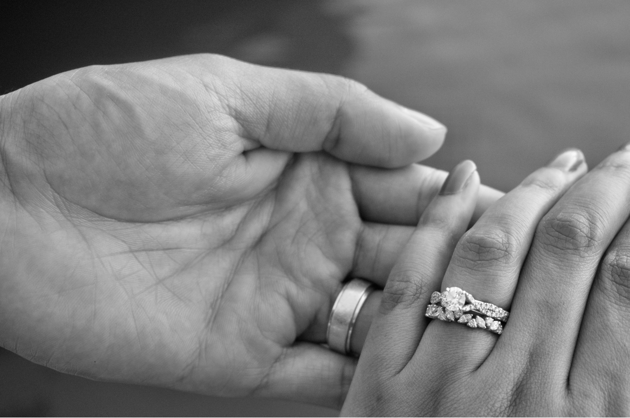 a lady wearing a round-cut engagement ring and wedding band holding a man’s hand a lady wearing a round-cut engagement ring and wedding band holding a man’s hand