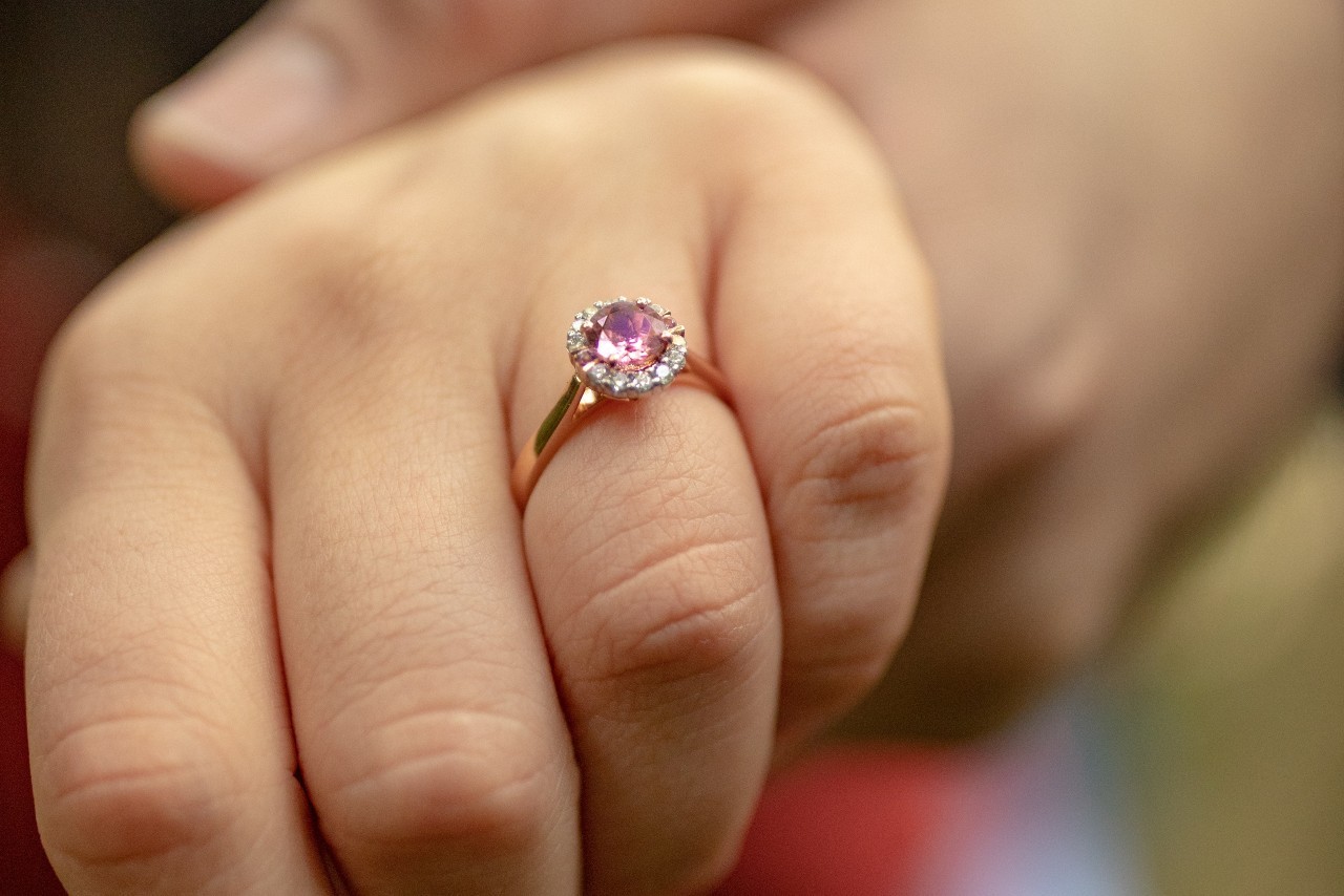 a woman’s hand adorned with a rose gold engagement ring with a purple centre stone a woman’s hand adorned with a rose gold engagement ring with a purple centre stone