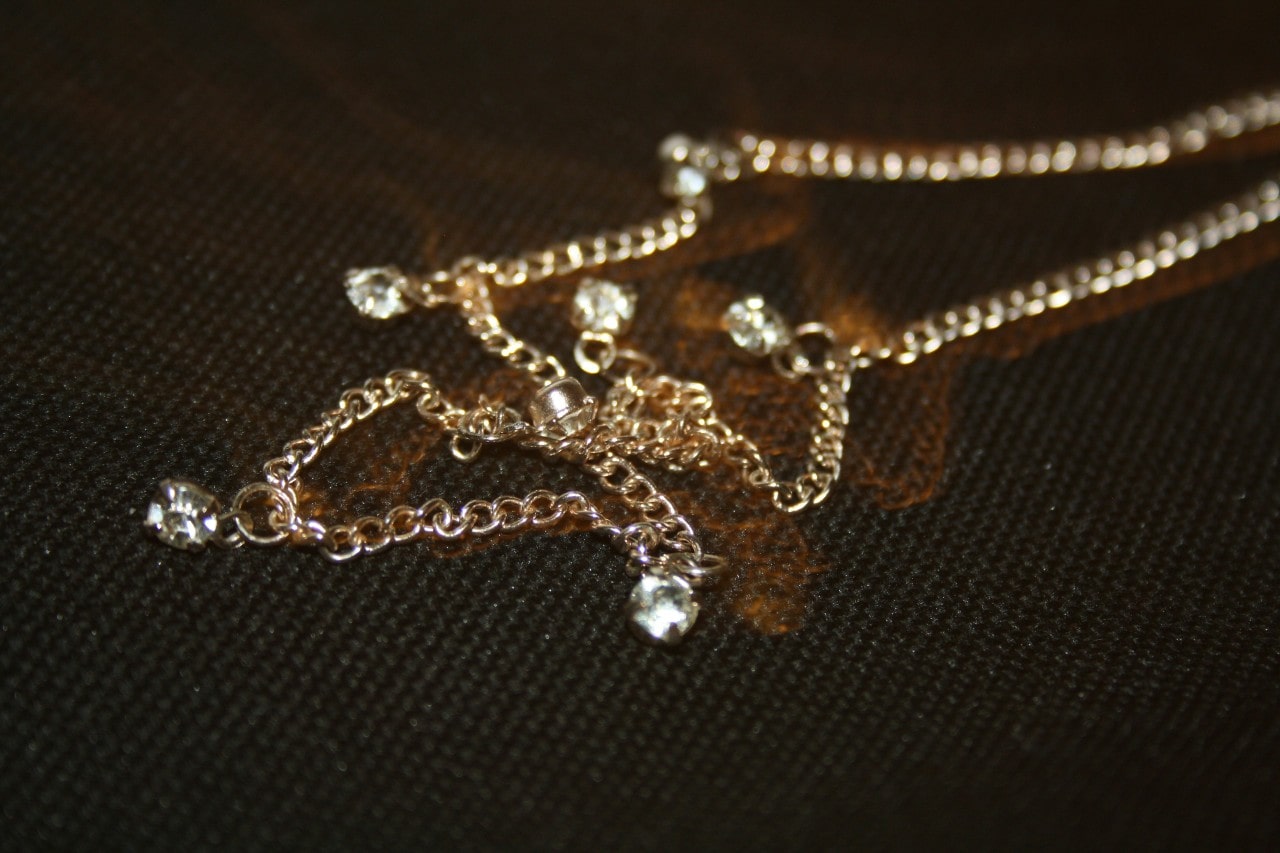 A close-up of a gold station necklace on a dark textured backdrop. A close-up of a gold station necklace on a dark textured backdrop.