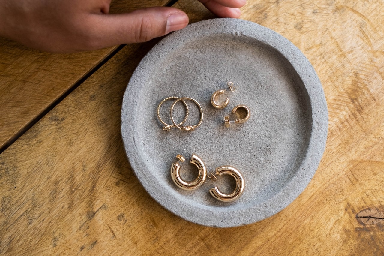 A cement dish holding three pairs of gold huggie earrings