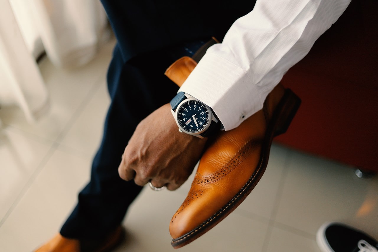 A man resting his wrist on his ankle and wearing a silver and blue watch