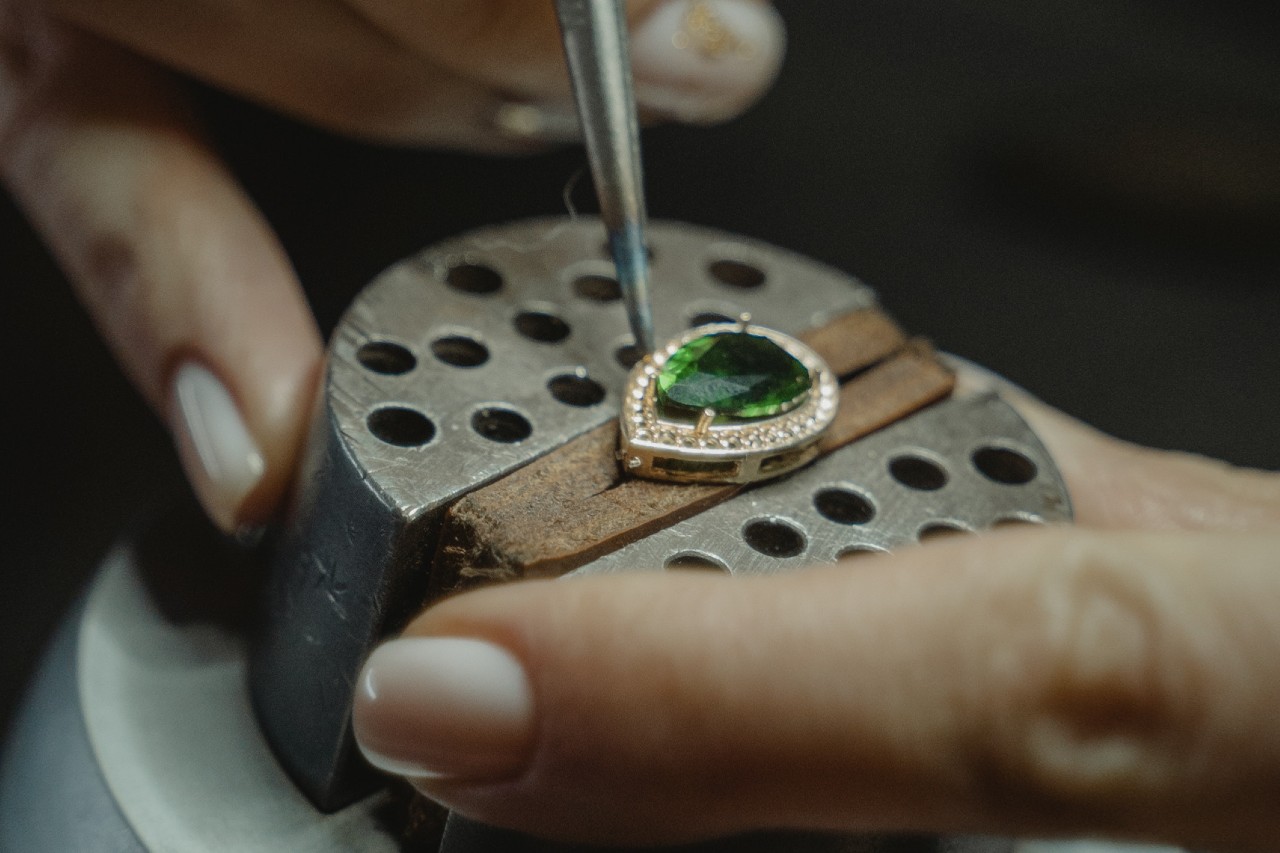 A jeweller places an emerald into a set of gold prongs
