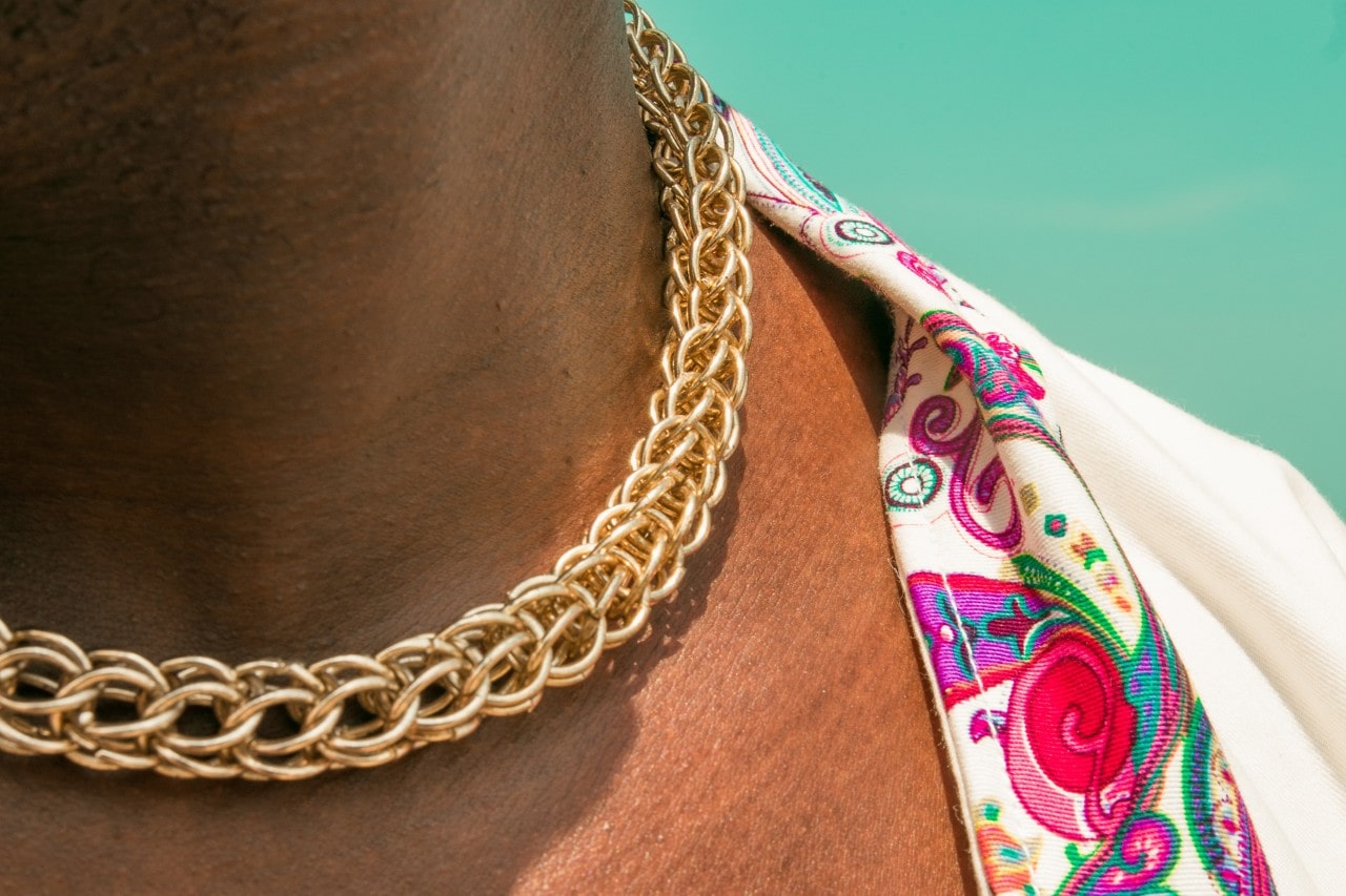 A close-up of a person wearing a yellow gold chain necklace contrasted by a colorful shirt. A close-up of a person wearing a yellow gold chain necklace contrasted by a colorful shirt.
