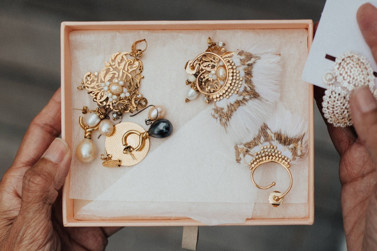 A close-up of a person holding a jewelry box with multiple pairs of intricate gold earrings. A close-up of a person holding a jewelry box with multiple pairs of intricate gold earrings.
